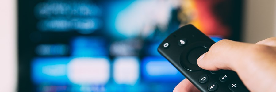 Hand on a FireTV remote in front of a blurred tv screen